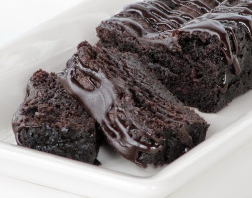 A closeup view of a Nigella Lawson's chocolate loaf cake with a chocolate drizzle glaze that has two pieces cut sitting in front of the remaining loaf.