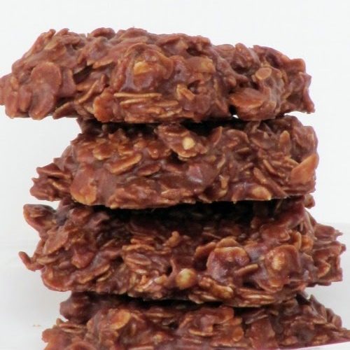 A stack of four chocolate peanut butter oatmeal no bake cookies are sitting on a white plate against a white background.