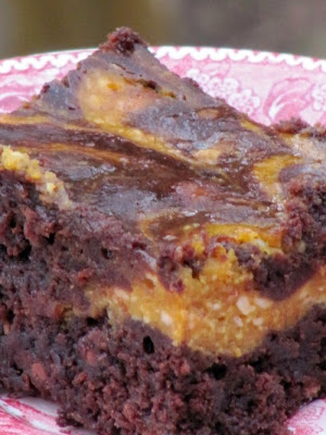 Closeup of a single chocolate pumpkin brownie made a with dark chocolate brownie topped with a layer of pumpkin cheesecake swirled with brownie batter on top. The bar is on a pink and white patterned plate.