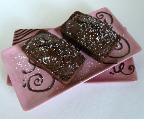 Two loaves of quadruple chocolate bread made with 4 kinds of chocolate chips, cocoa powder and chocolate chunks and dusted with chopped white chocolate are sitting on a rectangular pink tray balanced on another pink tray.