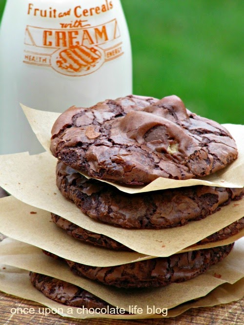 A closeup image of a tall stack of chocolate reeses peanut butter egg cookies separated with pieces of light brown parchment papers is sitting in front of a glass bottle filled with milk against a green background.