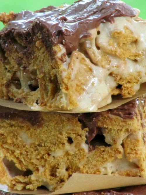 A close up of two rich gooey s'more cereal treats with melted marshmallows, graham cracker cereal and milk chocolate topping are stacked against a green background.