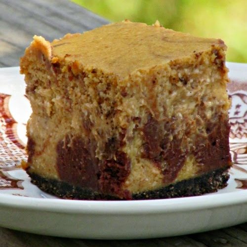 A closeup view of a square of chocolate pumpkin cheesecake made with pumpkin cheesecake with chocolate swirls on an oreo crust sitting on a white and brown plate.