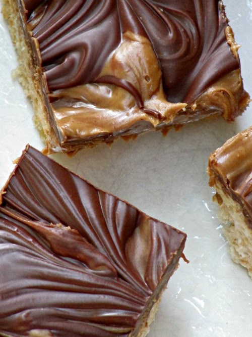 Overhead closeup view of the tops of three double peanut butter chocolate rice krispie treats with rich chocolate and peanut butter swirled frosted tops are shown against a white background surface.