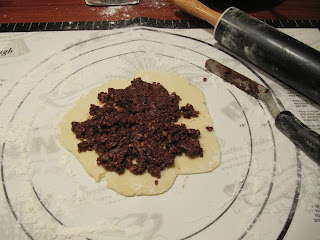 An overhead view of a round disk of chocolate cranberry rugelach cookie dough with a pile of chocolate, nut, and cranberry filling in the center.