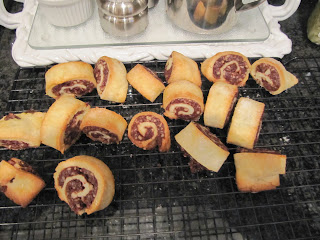 A pile of cinnamon roll shaped chocolate cranberry rugelach cookies are scattered on a cooling rack in front of a white tray.