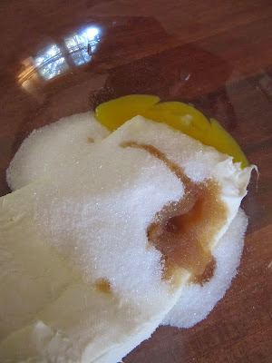 A closeup image of ingredients for the cream cheese layer of cream cheese brownies ready to be blended shows cream cheese, sugar and vanilla in a mixing bowl.