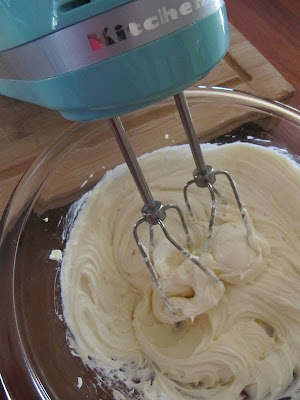 A blue stand mixer shows the cream cheese mixture ready for swirling into cream cheese brownies.