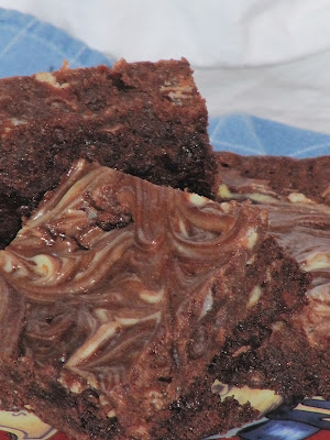 A stack of cream cheese brownie squares showing a swirl of cream cheese in the chocolate brownies is sitting on a blue cloth against a white background.