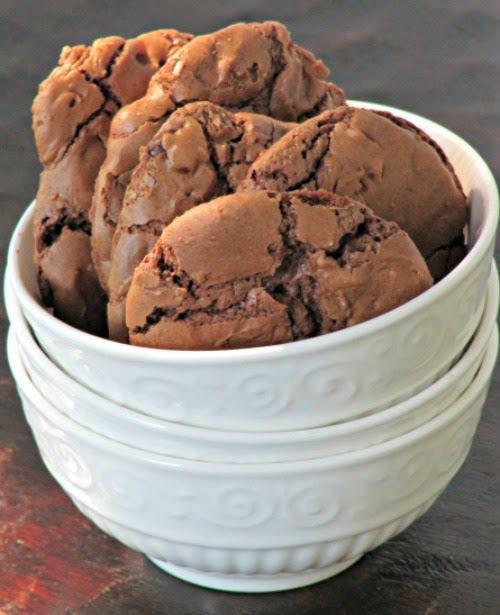 Side view of a stack of white bowls holding several large decadent chocolate brownie cookies with crackly surfaces.