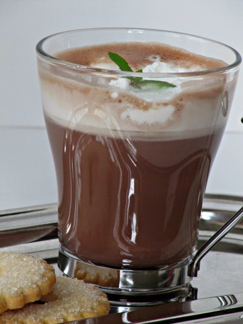 closeup side view of a tall glass mug of fresh basil mint hot chocolate drink on a tray with two sugar cookies.