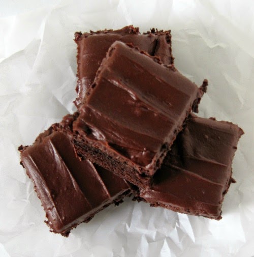 Overhead view of a pile of thick fudgy frosted brownies with thick fudge frosting sitting on crumpled white parchment paper.
