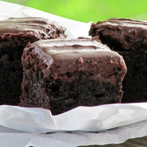 Closeup of three thick fudgy frosted brownies on white crumpled paper against a green background.