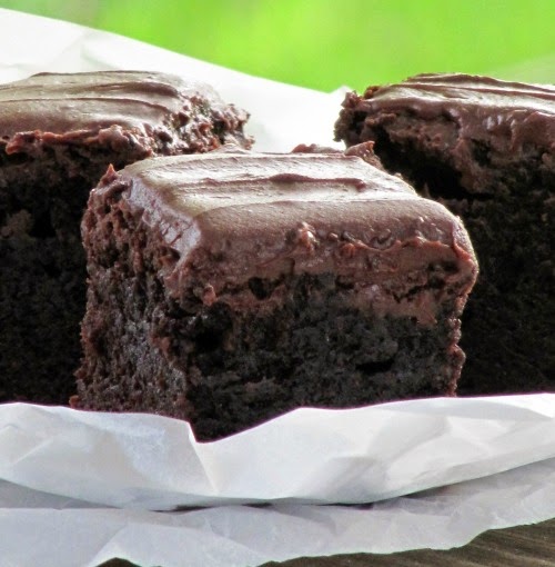 Closeup of three thick fudgy frosted brownies on white crumpled paper against a green background.