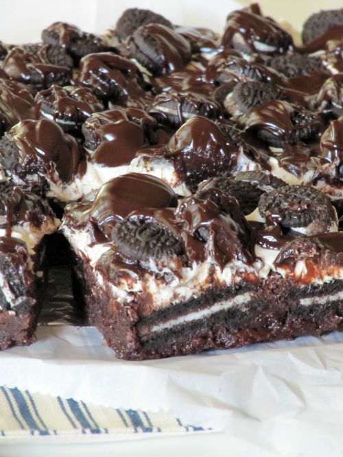 A close up of a slab of cookies and cream brownies made with chocolate brownies, Oreo cookies, marshmallow creme frosting, a chocolate glaze and topped with mini Oreos.