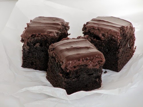 Three rich thick fudgy frosted brownies sitting on a piece of crumpled white parchment.