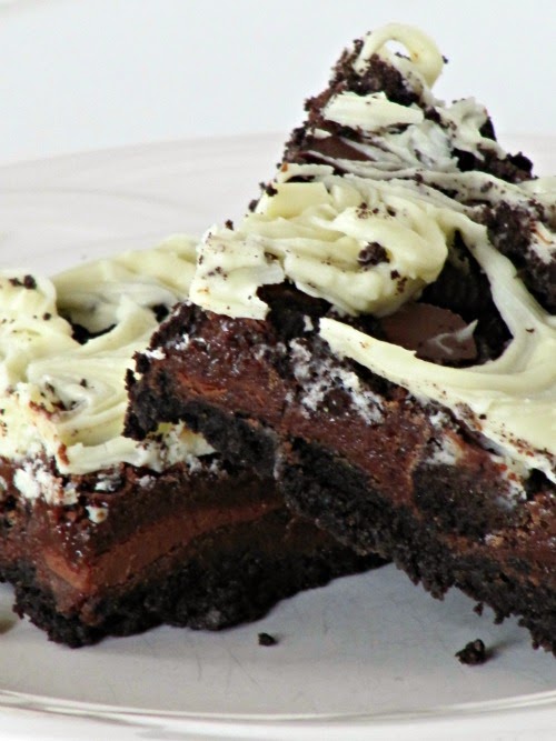 Two triple chocolate oreo bars are leaning against each other, each having an oreo crust, chocolate center, and chocolate and white cholate chip and oreo top layer, and are sitting on a white plate.