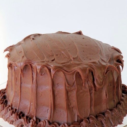 A closeup image of a round Hershey's perfectly chocolate cake frosted with Hershey's perfectly chocolate frosting with chocolate frosting garnish around the bottom edge of the cake..