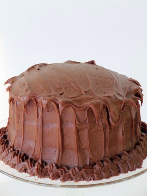 A closeup image of a round Hershey's perfectly chocolate cake frosted with Hershey's perfectly chocolate frosting with chocolate frosting garnish around the bottom edge of the cake..