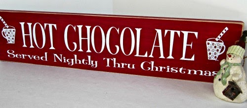 Red holiday signboard with white letters offering "hot chocolate served nightly thru christmas" behind a christmas snowman decoration, in prepaaration to make raspberry hot chocolate.