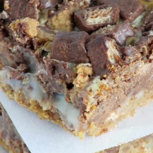 A closeup image of chocolate peanut butter chunk magic bars showing the graham cracker crumb layer, sweetened condensed milk, and the melted chocolate kit-kat and peanut butter cup candy on top.