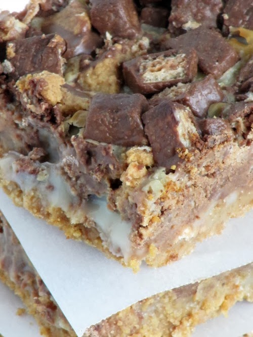 A closeup image of chocolate peanut butter chunk magic bars showing the graham cracker crumb layer, sweetened condensed milk, and the melted chocolate kit-kat and peanut butter cup candy on top.