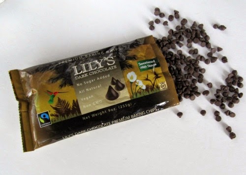 Image of an open dark brown bag of Lily's dark chocolate chips with chips spilling on a white surface.