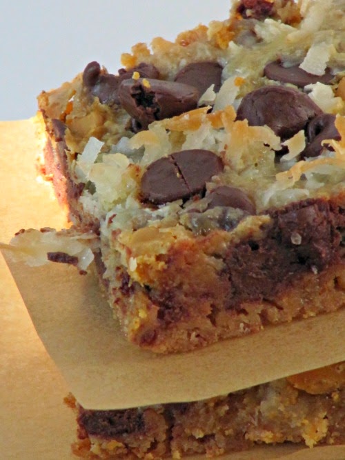 Close up of two pretzel peanut butter cup magic bars separated with a piece of parchment showing chocolate, graham cracker crust and held together with sweetened condensed milk.