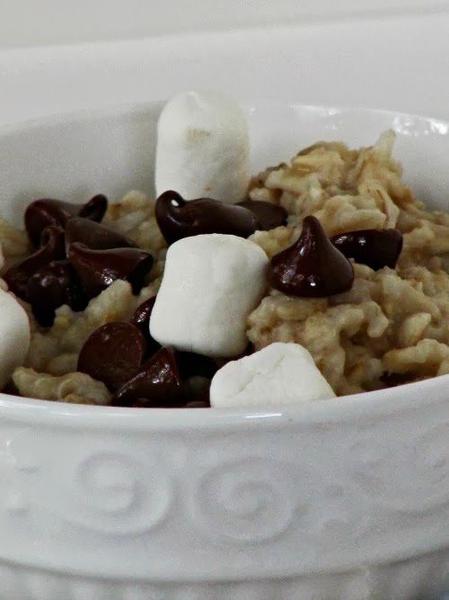 Closeup side view of a white bowl of s'mores oatmeal topped with mini-marshmallows and melting dark chocolate chips.