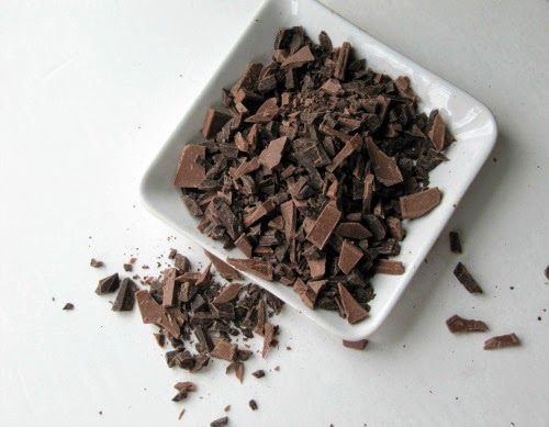 overhead view of square white tray holding dark chocolate chunks for making The hot chocolate Master Blend mix with a scattering of dark chocolate on a white surface.
