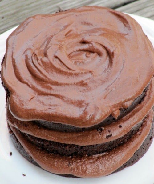 Closeup view of a three layer moist chocolate cake and fudge buttercream frosting on a white table.