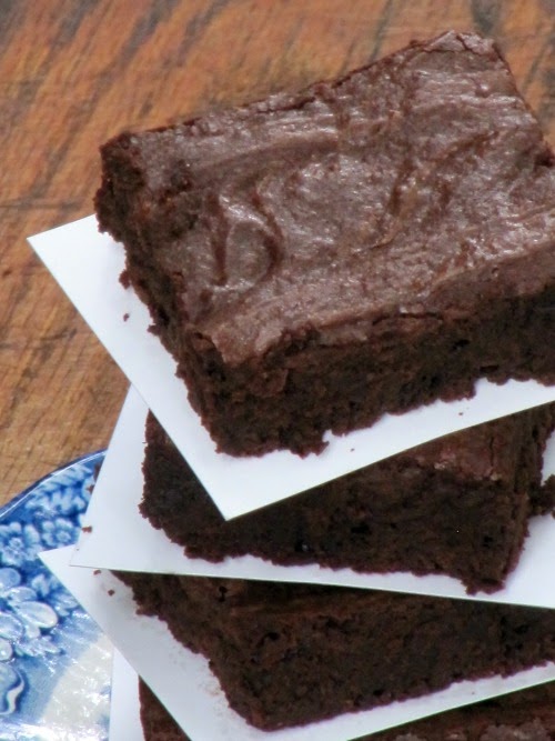 A closeup overhead view of a stack of the ultimate fudgy brownies made with dark cocoa powder and chocolate chips. The stack is separated by pieces of white parchment paper and is sitting on a blue floral rimmed plate on a brown wood table.
