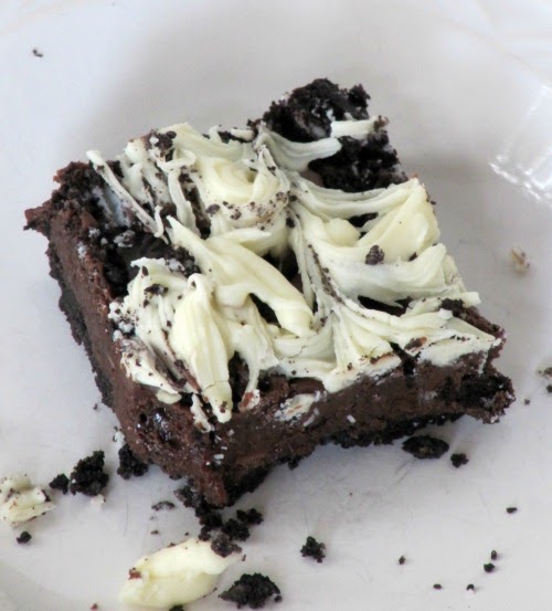 A top view of a single triple chocolate oreo bar sitting on a white plate with oreo crust crumbs surrounding the chocolate bar that has a creamy center and white chocolate swirls and oreo chunks on top.