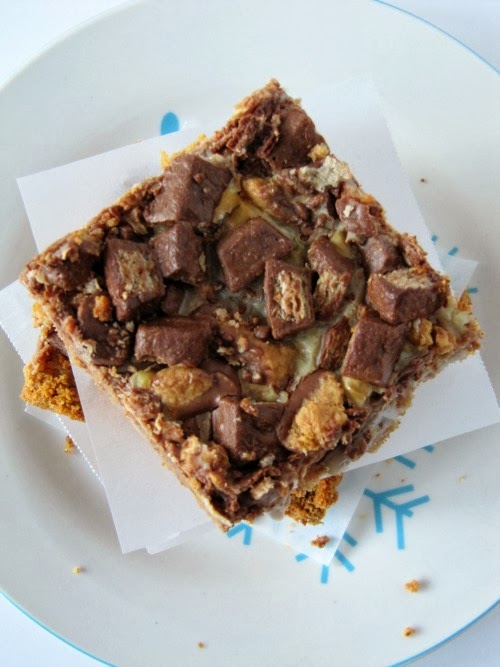 Top view of a stack of chocolate peanut butter chunk magic bars on a white plate with blue designs where you can see the top of one bar that shows chocolate melted kit-kat candy along with melted peanut butter cups.