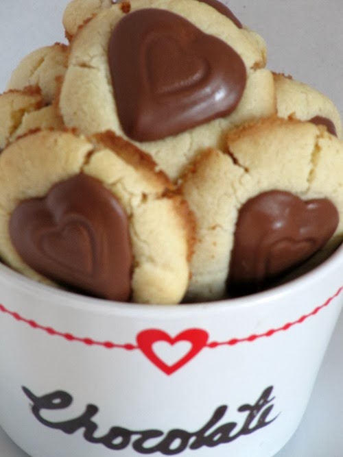A pile of valentine peanut butter heart thumbprint cookies made with buttery shortbread and chocolate peanut butter-filled heart-shaped candies are in a white dish that says "chocolate" in black and has a red heart on it.