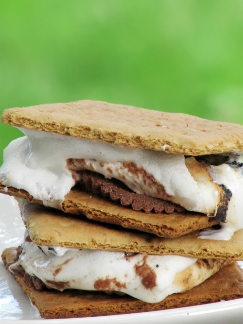 Image of two stacked Peanut butter cup s'mores made with graham crackers, marshmallows, and reese's peanut butter cups against a green background.