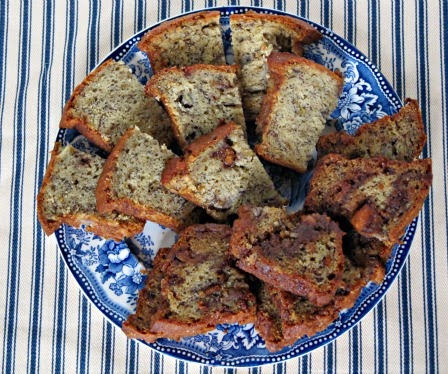 An overhead view of a large blue and white plate on a blue and white striped table covering, half holding sliced pieces of plain banana bread and the other half holding Reese's Peanut Butter Egg Banana Bread slices.