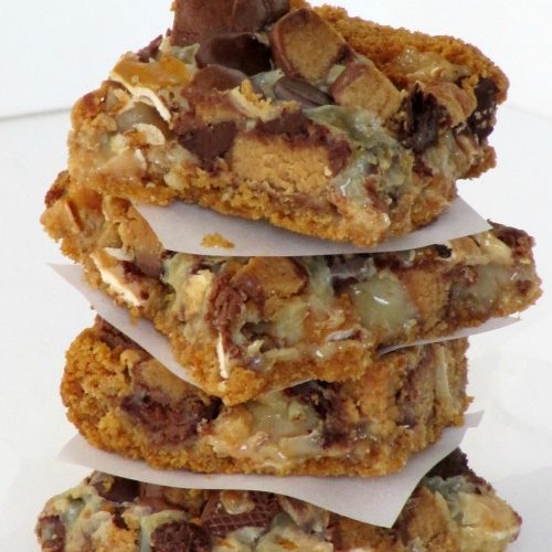 A stack of four pretzel peanut butter cup magic bars sits on a white surface against a white background.
