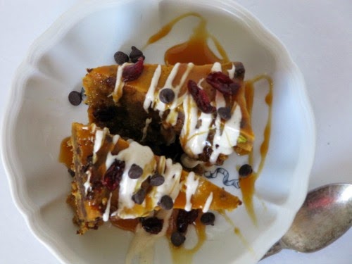 An overhead view of two triangles of Pumpkin Bread Pudding with Lily's Dark Chocolate, Cranberries and White Chocolate Drizzleon a white surface.