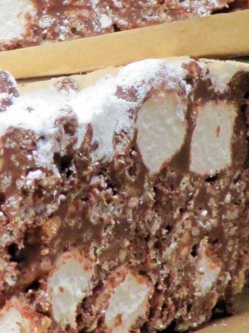 Closeup on a side view of a rich puppy chow rice krispie treat that shows chocolate and peanut butter with rice krispies and marshmallows and topped with powdered sugar.