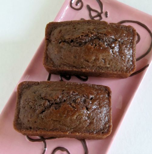 Ovverhead view of two loaves of Quadruple Chocolate Bread made with cocoa powder, milk, white, and dark chocolate chips plus dark chocolate chunks, sitting on a pink rectangular tray with brown writing on it.