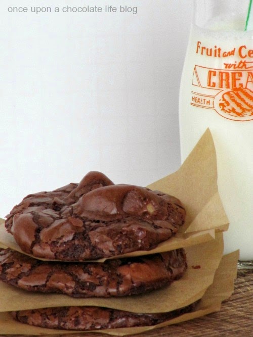 A stack of chocolate reeses peanut butter egg cookies separated with pieces of light brown parchment paper is sitting in front of a glass bottle filled with milk against a white background.