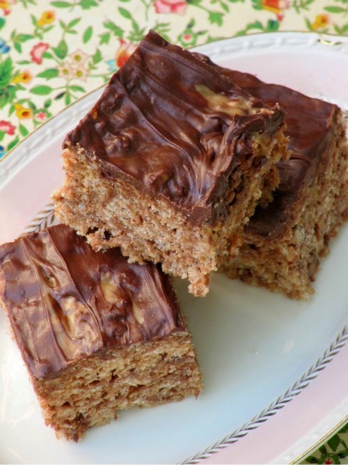 Overhead view of three Reese's Peanut Butter Cup Rice Krispies treats on an oval white platter against a multicolored floral table covering.