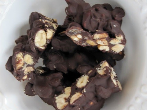 Cloweup image of pieces of chocolate covered salted caramel peanut bark showing peanuts, dark chocolate and caramel, in a white dish.