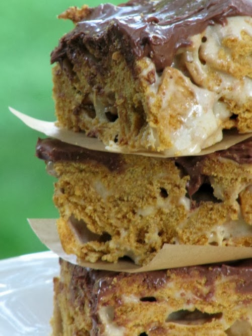A stack of three s'more cereal treats made with graham cracker cereal, chocolate, and marshmallows is sitting on a white plate against a green background.