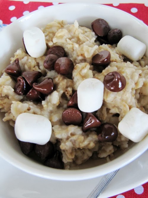 Closeup overhead view of a bowl of s'mores oatmeal topped with molten chocolate chips, mini-marshmallows and graham cracker crumbs on a red and white polka dot background.