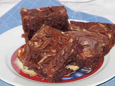 A plate of cream cheese brownies with swirled cream cheese is sitting on a blue cloth on a white table.