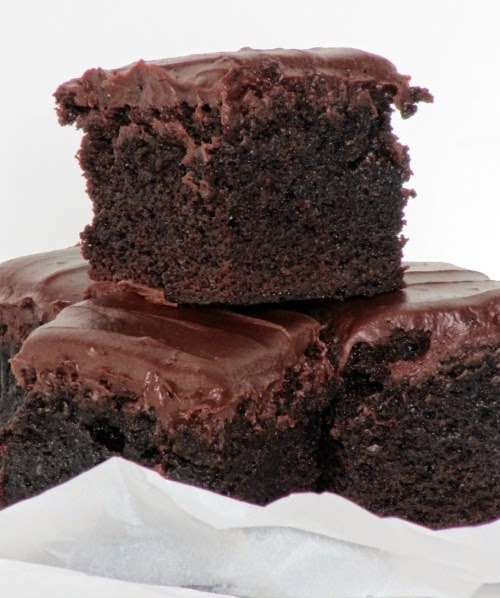A side view of four deep chocolate thick fudgy frosted brownies sitting on a piece of crumpled white parchment paper.