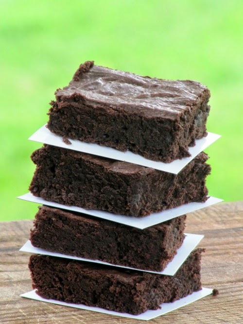 A stack of the ultimate fudgy brownies that are moist and deep chocolate with crispy tops is on a wood table against a green background.