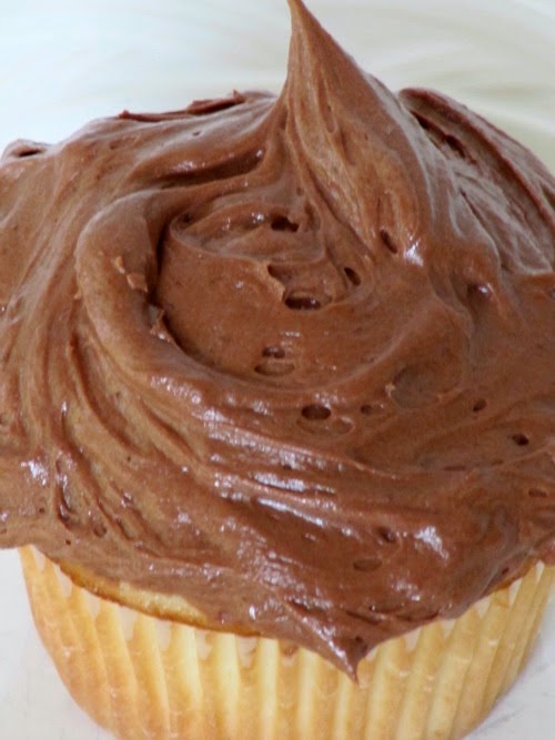 A closeup overhead view of a moist vanilla cupcake with mocha buttercream shown against a white background.